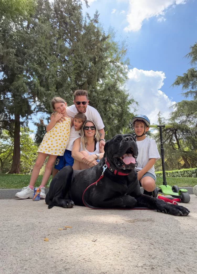 A family gathered around their large black dog in a park
