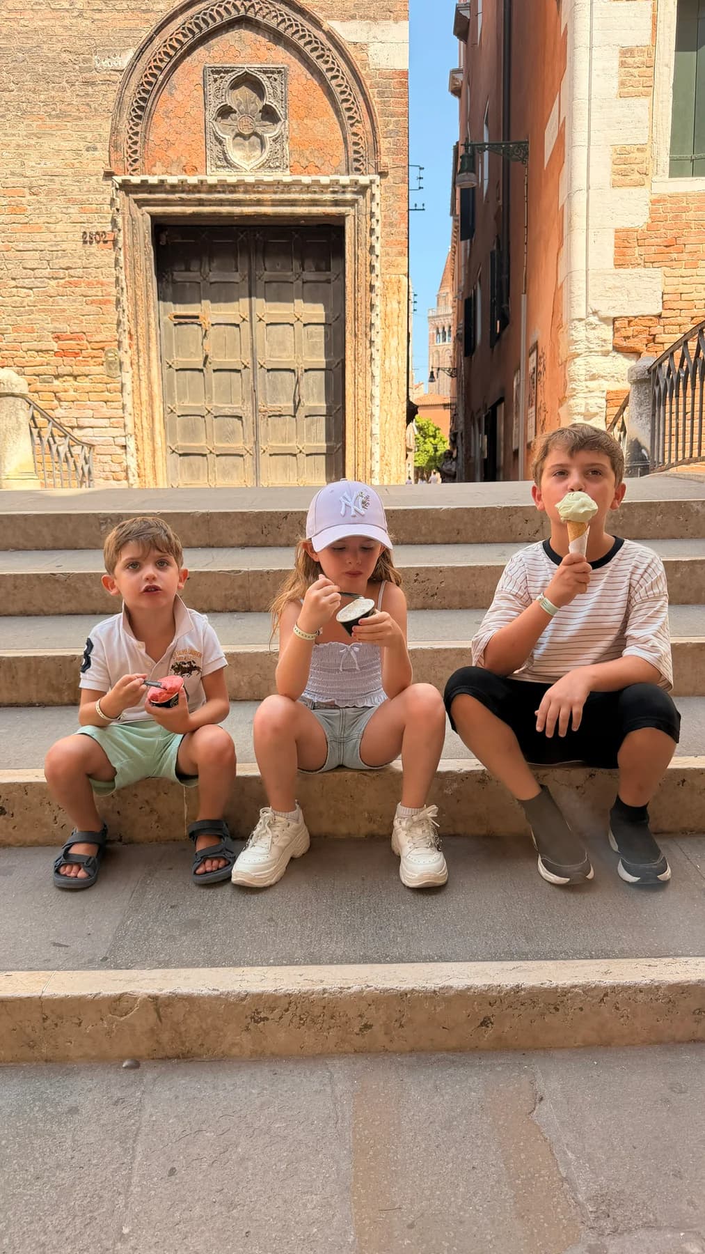Three children eating gelato together on stone steps